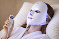 Person wearing a LED face mask with remote control on a beige background