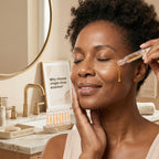 Woman applying a skincare product to her face with a mirror and skincare items in the background