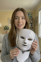 Woman holding a white mask in a room with a couch and decor.