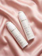Two white Theobion Barrier Cushion pump bottles arranged diagonally on a draped pink satin fabric background.