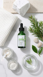 Green bottle with dropper on a white surface with jars, leaves, and soap.